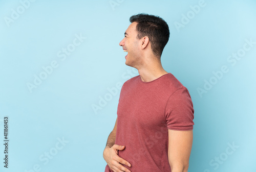 Young caucasian handsome man isolated on blue background laughing in lateral position