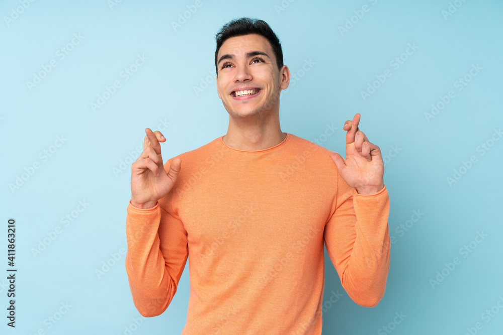 Young caucasian handsome man isolated on blue background with fingers crossing and wishing the best Young caucasian handsome man isolated on blue background with fingers crossing and wishing the best