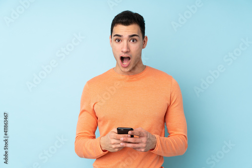 Young caucasian handsome man isolated on blue background surprised and sending a message