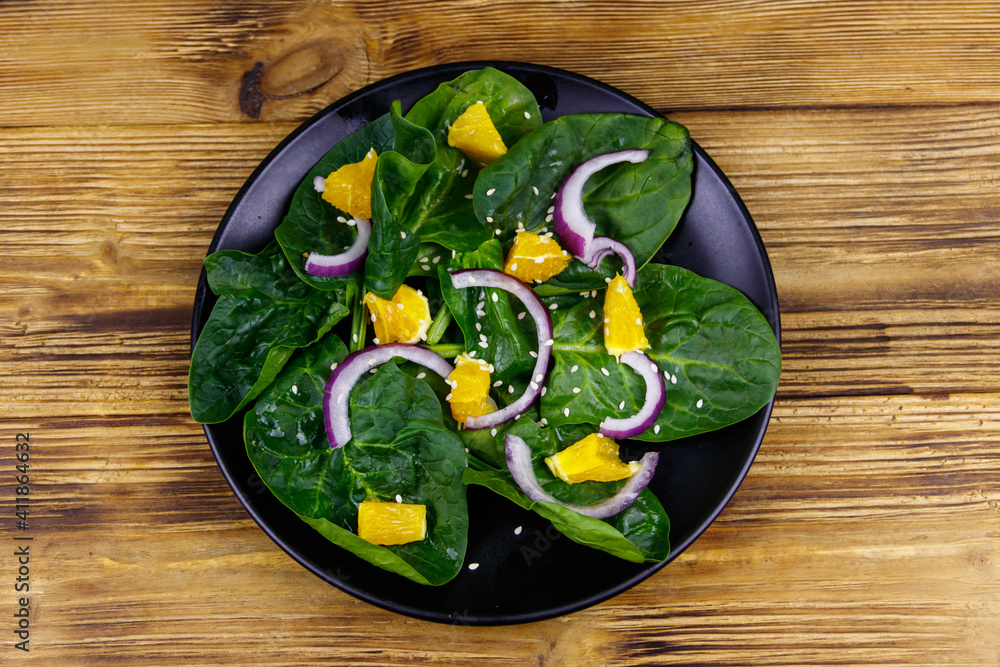 Tasty salad with spinach, orange, red onion and sesame seeds on wooden table. Top view. Healthy food or vegetarian concept