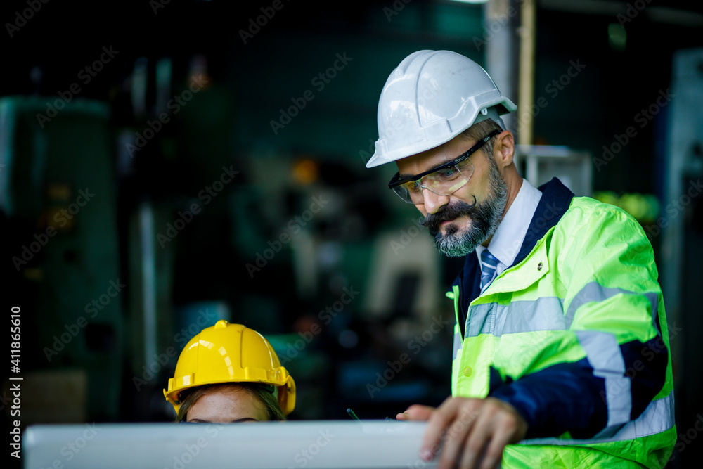 Chief engineer is watching young female engineer work at the machine industrial. He is standing next to her who using the personal computer. Chief engineer is watching young female engineer work at the machine industrial. He is standing next to her who using the personal computer.