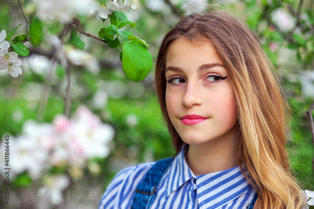 Pretty teen girl are posing in garden near blossom tree with white flowers. Spring time
