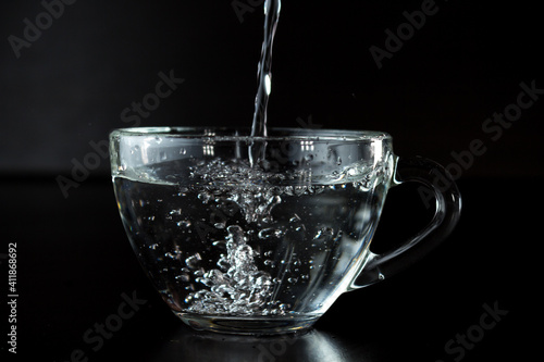 pouring water into a glass. transparent cup with water on a dark background.