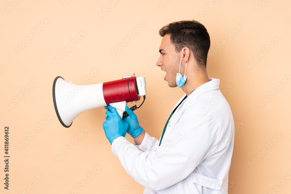 Young dentist man holding tools isolated on beige background shouting through a megaphone Young dentist man holding tools isolated on beige background shouting through a megaphone