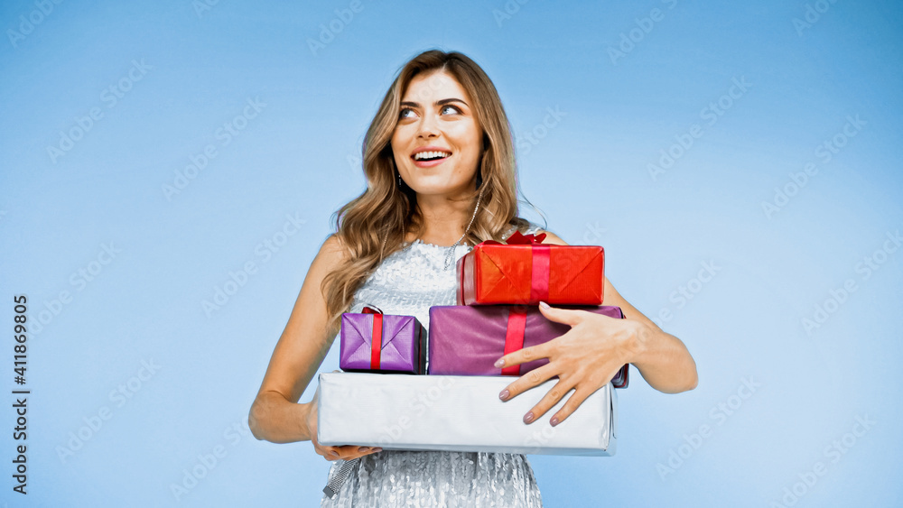 Fototapeta premium happy woman with curly hair holding wrapped presents on blue