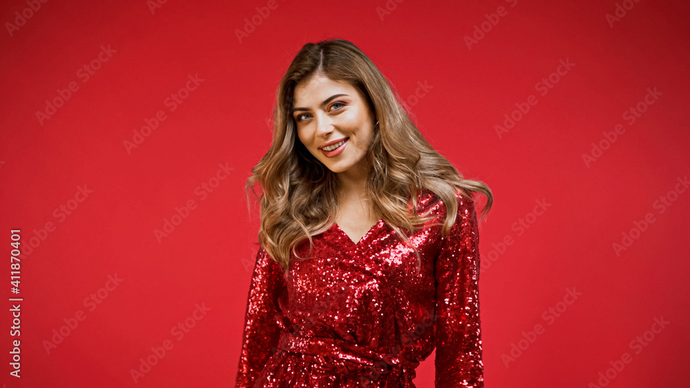 positive woman in shiny dress looking at camera isolated on red positive woman in shiny dress looking at camera isolated on red