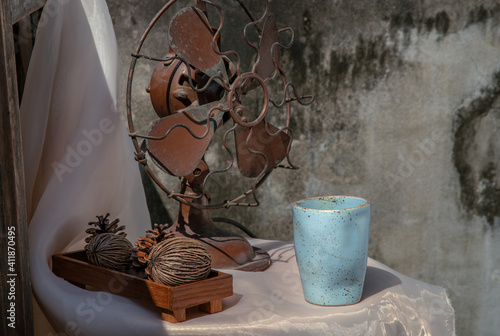 Old vintage brown metal fan and Dried cerbera oddloam's with Blue ceramic mug handmade on pink table with old ruins cement wall. Selective focus. photo