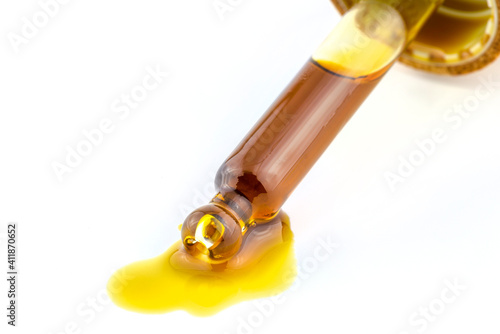 A macro shot of a glass pipette and a drop of CBD oil from cannabis extract, isolated on white.