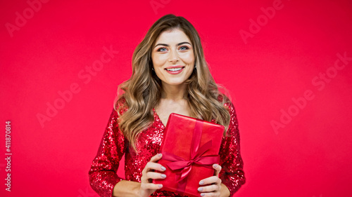 happy woman with wavy hair holding present isolated on red