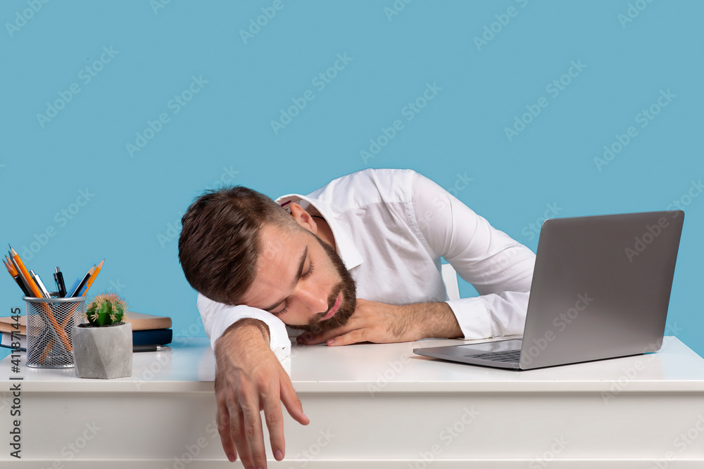 Exhausted young businessman sleeping on his desk, tired of overworking on blue studio background, copy space Exhausted young businessman sleeping on his desk, tired of overworking on blue studio background, copy space
