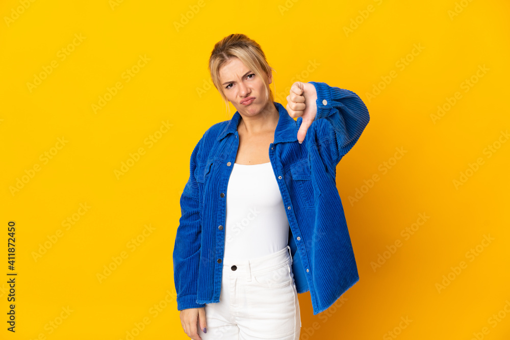 Young Russian woman isolated on yellow background showing thumb down with negative expression Young Russian woman isolated on yellow background showing thumb down with negative expression