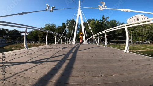 Rear view of woman riding electric scooter across bridge in Kharkiv Strelka park, Ukraine
