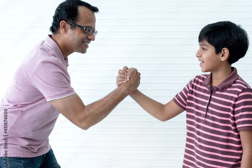 Indian father enjoying leisure time at home, Indian father and son competing in arm wrestling on white background Indian father enjoying leisure time at home, Indian father and son competing in arm wrestling on white background