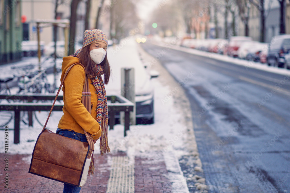 Midde-aged brunette woman standing at a bus stop, wearing a protective face mask due to corona virus, waiting for her bus to bring her to work Midde-aged brunette woman standing at a bus stop, wearing a protective face mask due to corona virus, waiting for her bus to bring her to work