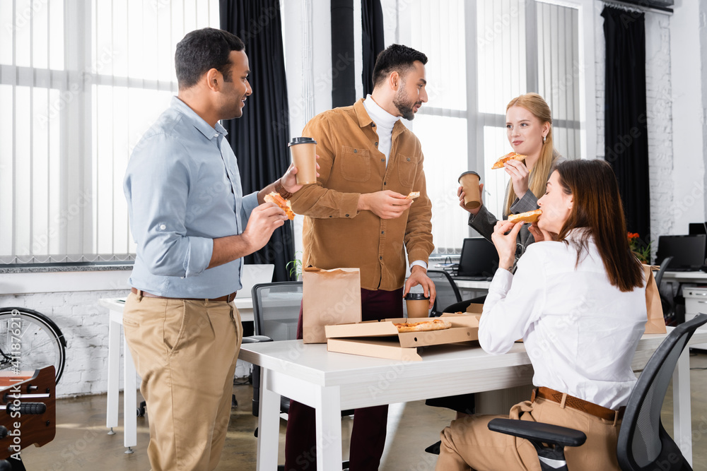 Multiethnic business people eating pizza and holding coffee to go during lunch Multiethnic business people eating pizza and holding coffee to go during lunch