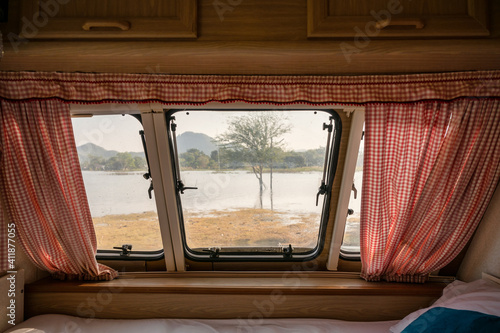 Inside of empty bed in camper van and the view through window with curtain on lakeside