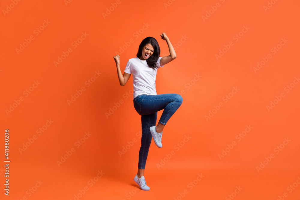 Full length photo of lady open mouth raise fist knee wear white t-shirt jeans sneakers isolated orange color background - obrazy, fototapety, plakaty 