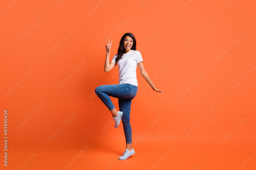 Full length photo of lady show v-sign open mouth wear white t-shirt jeans footwear isolated orange color background Full length photo of lady show v-sign open mouth wear white t-shirt jeans footwear isolated orange color background