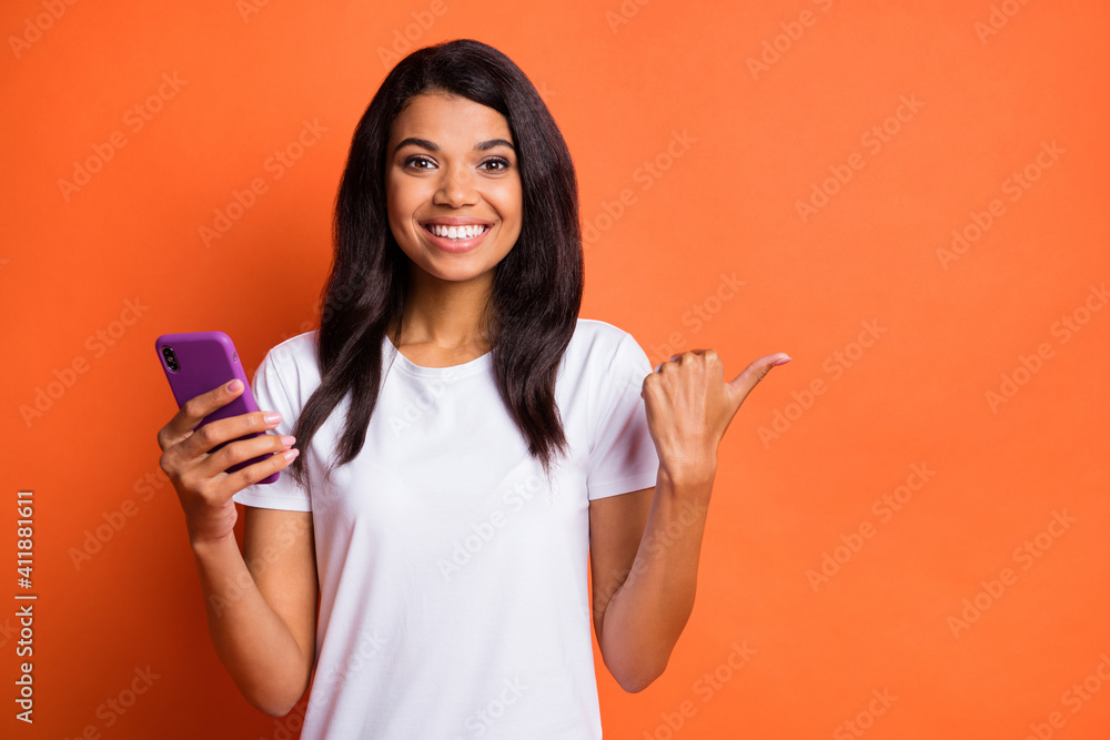 Photo of lady hold phone direct thumb empty space wear white t-shirt isolated orange color background Photo of lady hold phone direct thumb empty space wear white t-shirt isolated orange color background