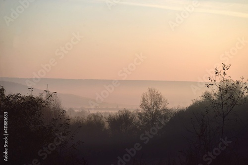sunrise with fog in the forest colored in green and yellow. early autumn landscape in the wild © badescu