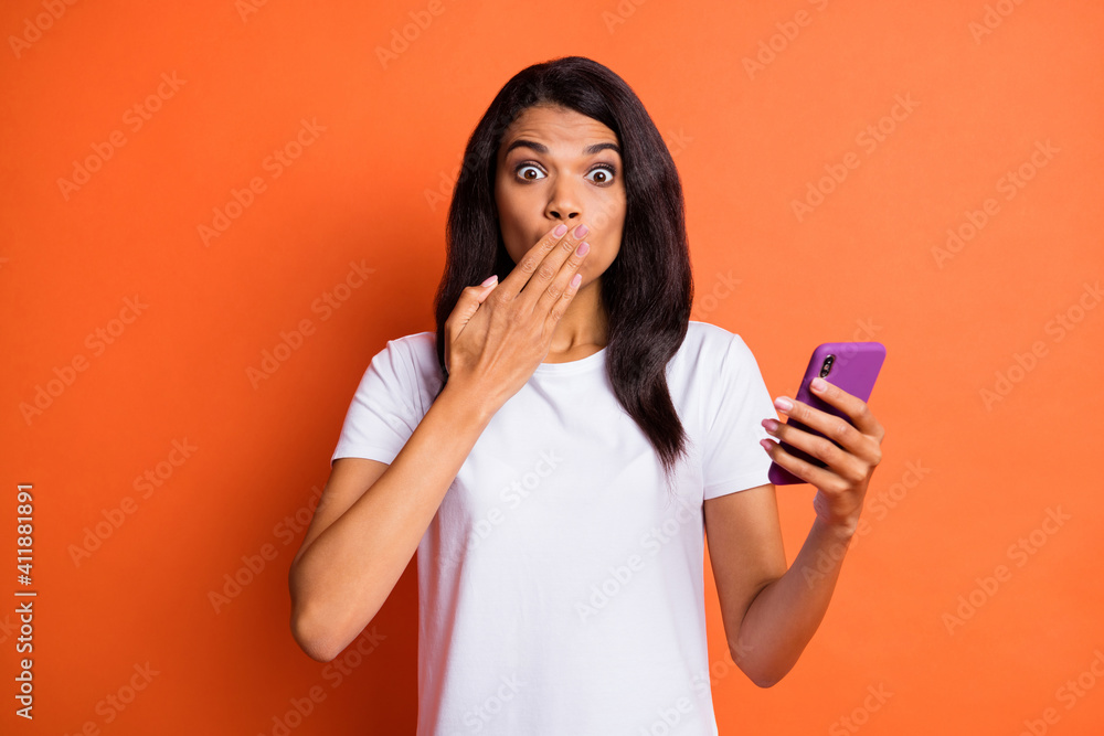 Photo of girl hold telephone palm close mouth staring camera wear white t-shirt isolated orange color background