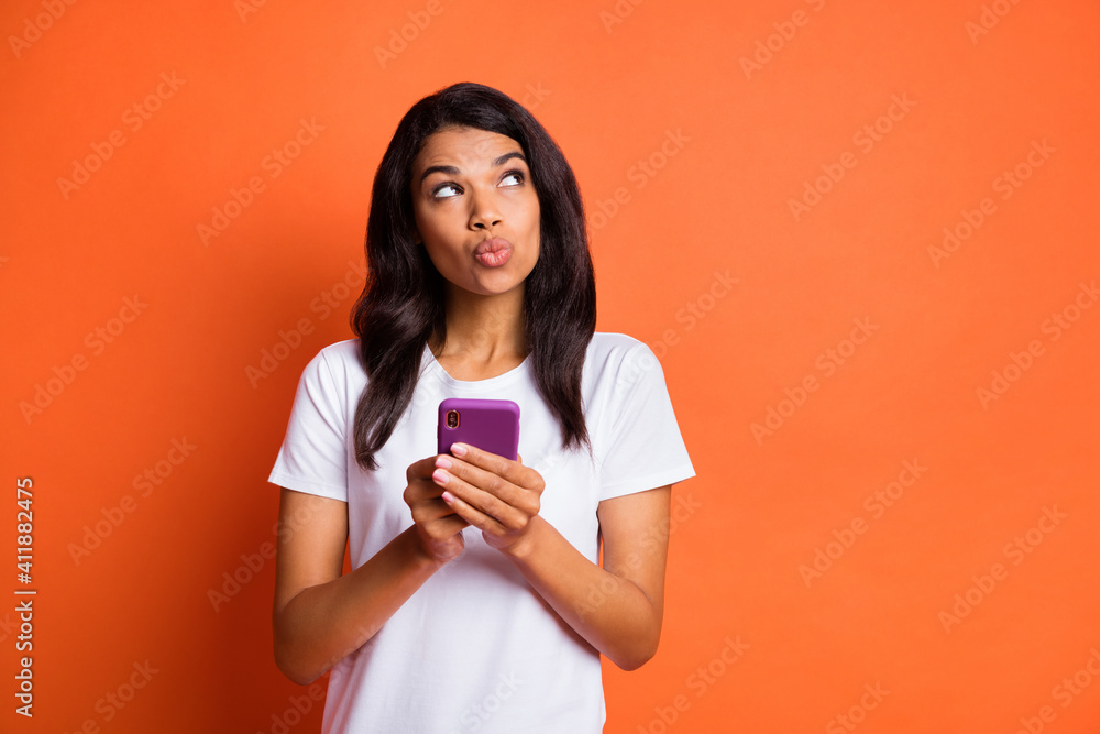 Photo of dreamy lady hold phone look up empty space wear white t-shirt isolated orange color background Photo of dreamy lady hold phone look up empty space wear white t-shirt isolated orange color background