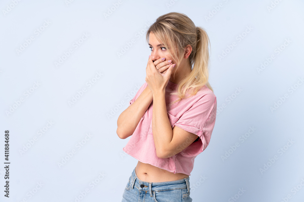 Blonde woman over isolated blue background covering mouth and looking to the side Blonde woman over isolated blue background covering mouth and looking to the side
