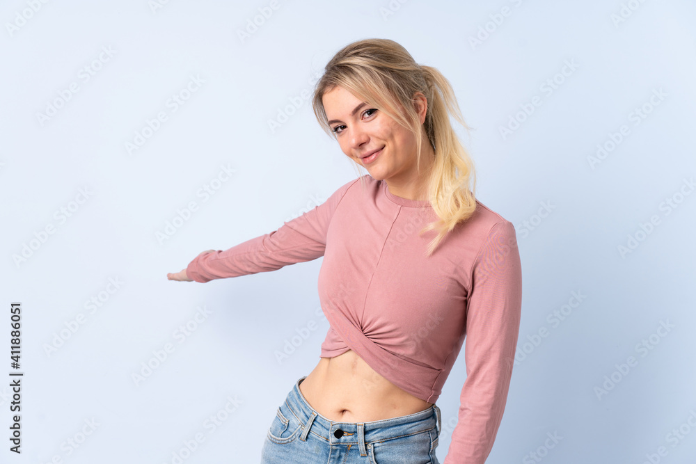 Blonde woman over isolated blue background extending hands to the side for inviting to come Blonde woman over isolated blue background extending hands to the side for inviting to come