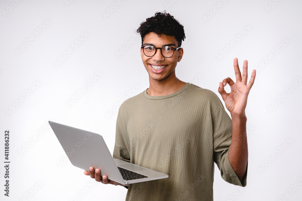 Happy young mixed-race student showing okay sign using laptop isolated over white background Happy young mixed-race student showing okay sign using laptop isolated over white background