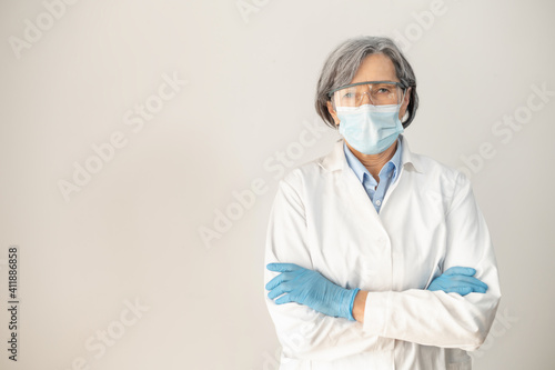 Senior female doctor medical robe, protective goggles, face mask, and latex gloves, crossing arms and posing isolated over gray background, fully equipped health professional working during pandemic © Vadim Pastuh