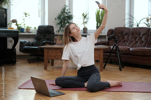 Joyful woman in sportswear poses on camera in modern apartment with photocamera and some stylish furniture.