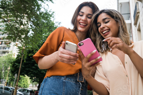 Two friends using mobile phone outdoors.