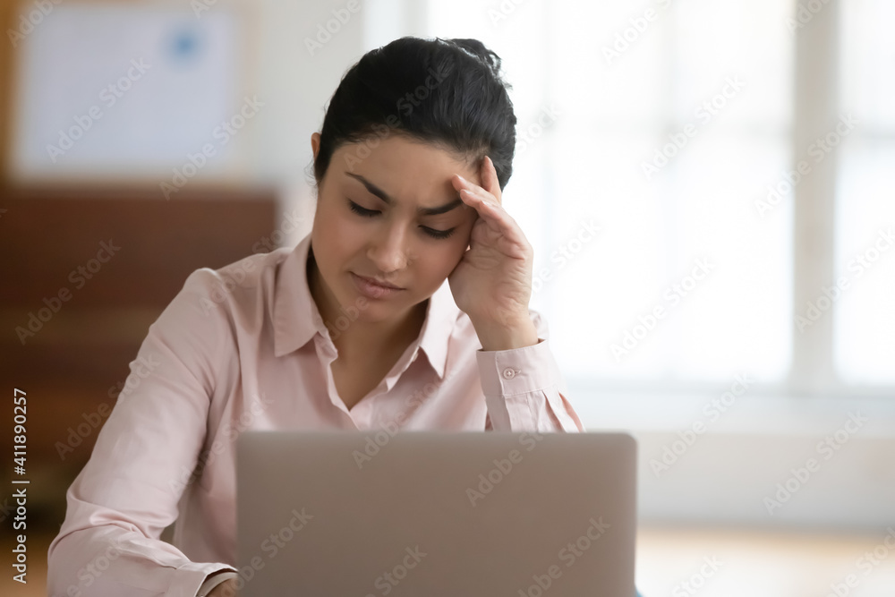 Upset unhappy female employee getting bad news at workplace. Desperate tired young Indian business woman with laptop suffering from headache, feeling dizzy and exhausted. Stress and problem at work Upset unhappy female employee getting bad news at workplace. Desperate tired young Indian business woman with laptop suffering from headache, feeling dizzy and exhausted. Stress and problem at work
