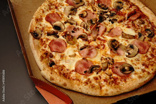 Pizza in a box on a black background. With cheese and mushrooms. Top view.