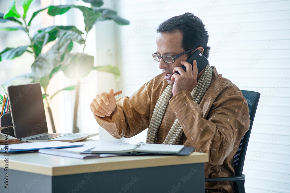 Serious Indian business man in traditional clothes using smartphone while working in office, busy working Serious Indian business man in traditional clothes using smartphone while working in office, busy working