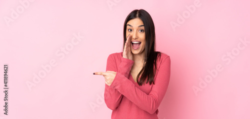 Young caucasian woman over isolated background pointing to the side to present a product and whispering something
