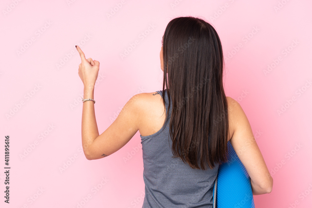 Young caucasian woman with mat isolated on pink background pointing back with the index finger Young caucasian woman with mat isolated on pink background pointing back with the index finger