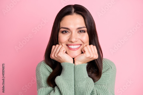 Photo of charming young girl fists hold cheeks toothy smile wear green cardigan isolated pastel pink color background