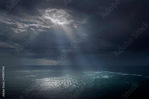 Dramatic scenery. Lightbeams. Sunbeams. Biblical religious atmosphere. Dark clouds. Cape Reinga. Pacific Ocean. Tasman Sea. Coast. Rain coming up. New Zealand