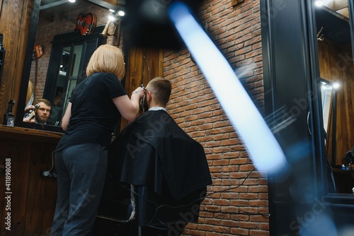 Stylish man sitting barber shop Hairstylist Hairdresser Woman cutting his hair Portrait handsome happy young bearded caucasian guy getting trendy haircut Attractive barber girl working serving client