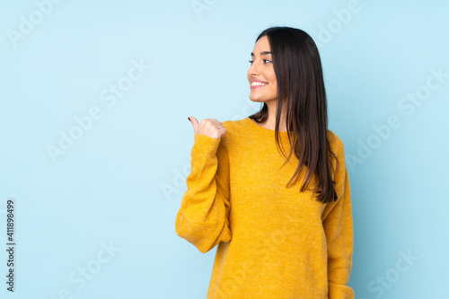 Young caucasian woman isolated on blue background pointing to the side to present a product