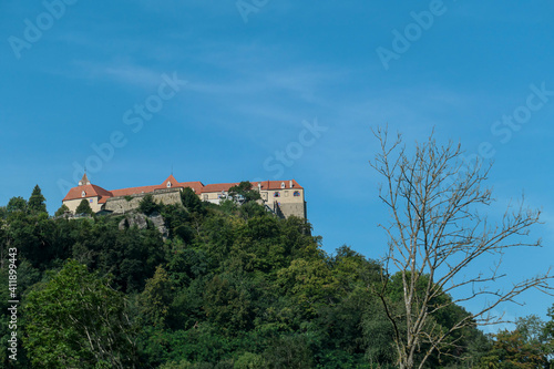 Riegersburg castle in Austria towering above the area. Dense forest overgrowing the rock. Clear blue sky above the castle. The massive fortress built on the rock. Defensive structure from middle ages