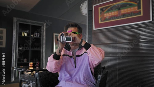 An unusual freaky guy from the 80s or 90s in purple clothes, in his hand he has an old video camera that works from a tape cassette.