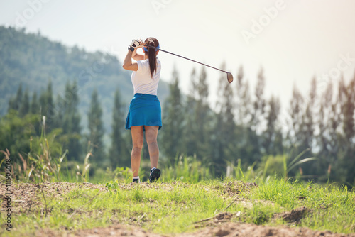 Woman golfer finished golf swing. Close up of female golf player swinging golf club on fairway during day time.
