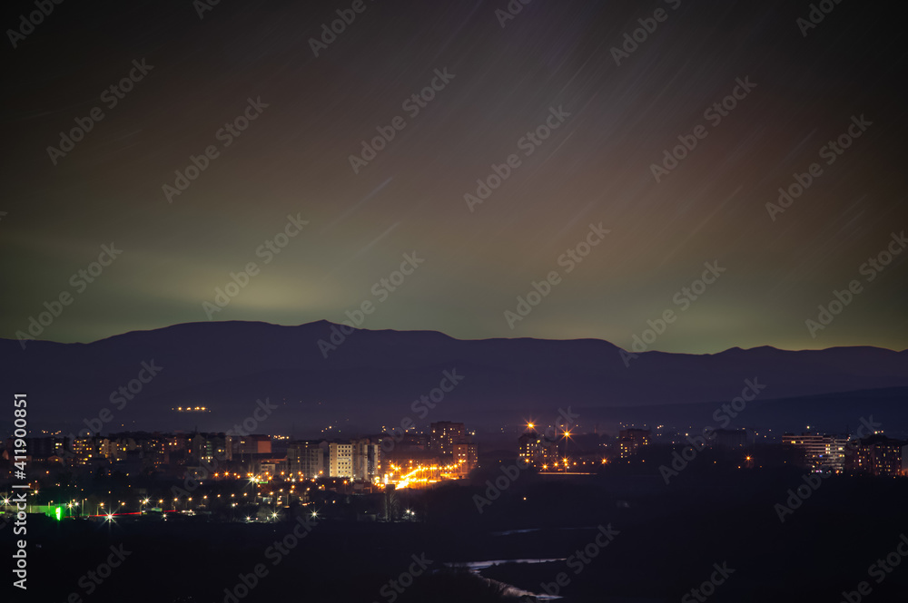 Traces of stars in the sky against the background of mountains and the city of Ivano-Frankivsk