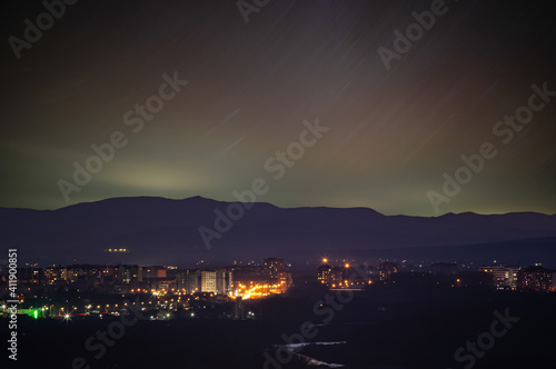 Traces of stars in the sky against the background of mountains and the city of Ivano-Frankivsk