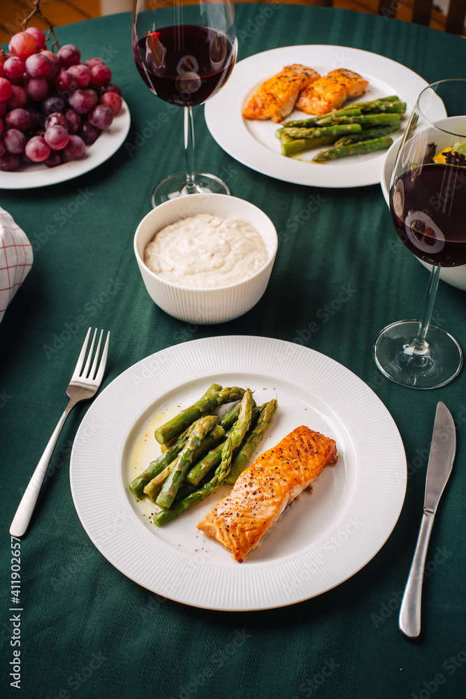 European cuisine. Salmon steak with asparagus, vegetable salad, sauce, grapes and bread with glasses of red wine. Dinner for two in the kitchen