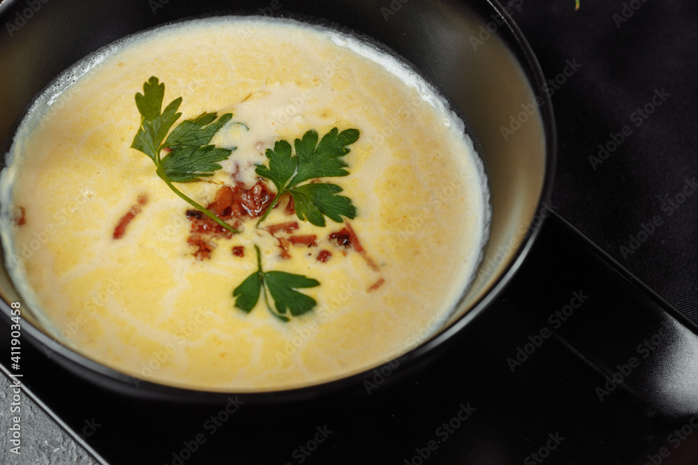 Cheese soup in a black plate on gray background