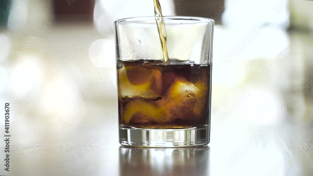 The drink is poured into a glass with ice The drink is poured into a glass with ice