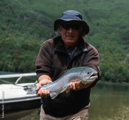 1 big man fisherman holding a rainbow fish smiling and looking at the camera